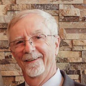 A man with white hair and glasses is smiling.